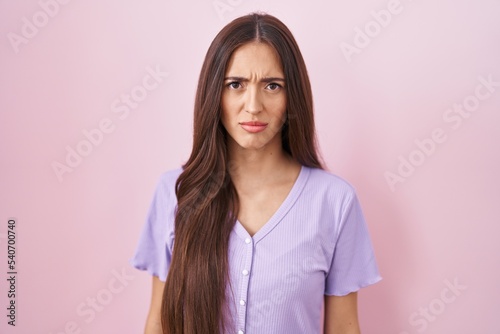 Young hispanic woman with long hair standing over pink background skeptic and nervous, frowning upset because of problem. negative person.