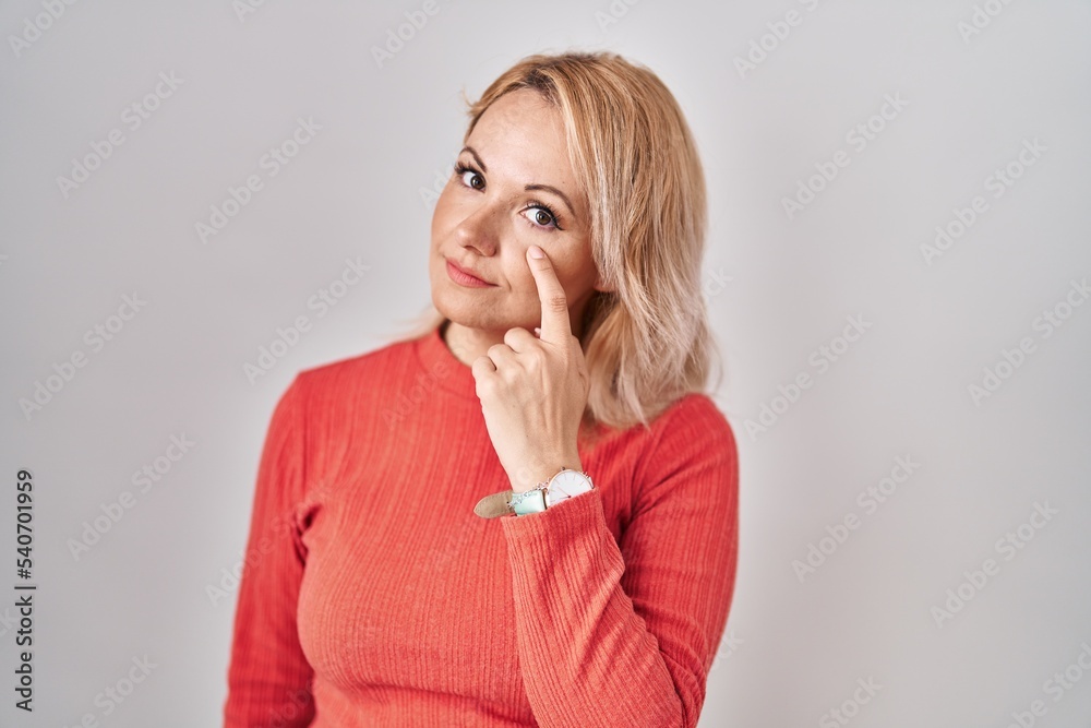 Blonde woman standing over isolated background pointing to the eye watching you gesture, suspicious expression Blonde woman standing over isolated background pointing to the eye watching you gesture, suspicious expression