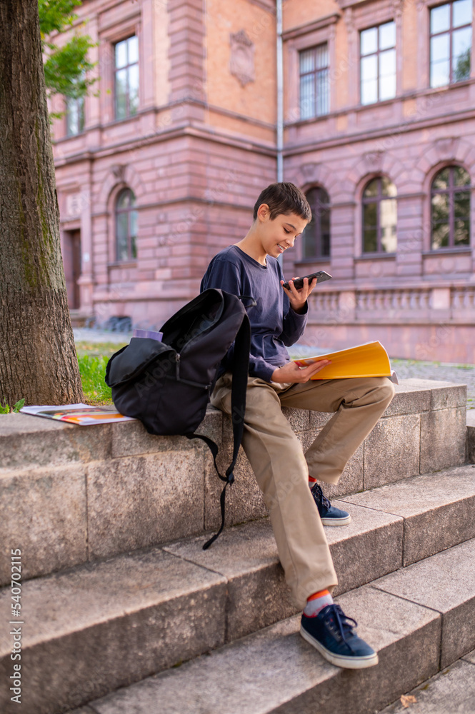 Obraz premium Joyous teen seated on the stairs outdoors using his cellphone