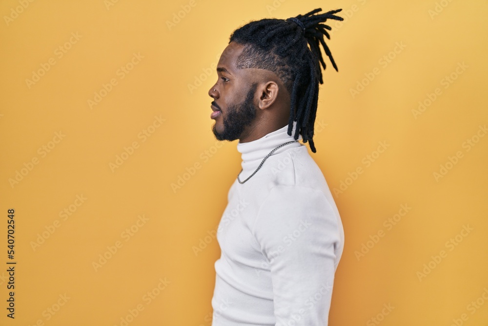 Fototapeta premium African man with dreadlocks wearing turtleneck sweater over yellow background looking to side, relax profile pose with natural face and confident smile.