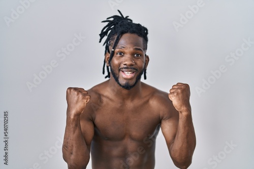 African man with dreadlocks standing shirtless over isolated background screaming proud  celebrating victory and success very excited with raised arms