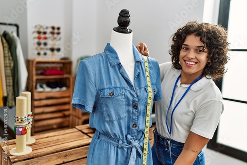 Young latin shopkeeper woman smiling happy measuing clothes on manikin at clothing store. photo