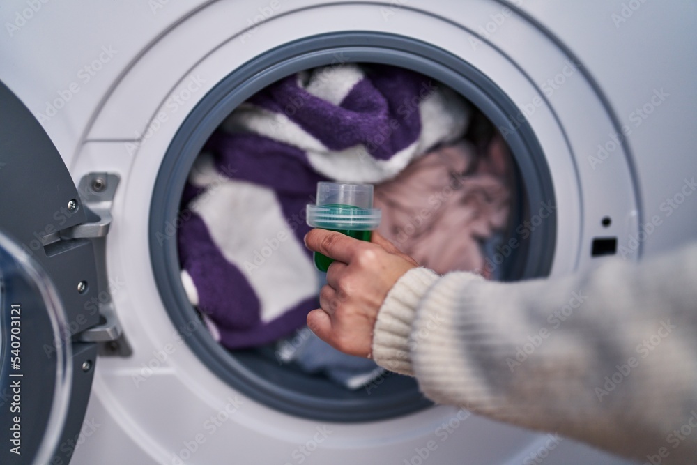Young beautiful hispanic woman pouring detergent on washing machine at laundry room Young beautiful hispanic woman pouring detergent on washing machine at laundry room