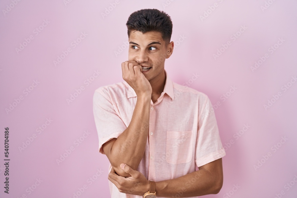Young hispanic man standing over pink background looking stressed and nervous with hands on mouth biting nails. anxiety problem. Young hispanic man standing over pink background looking stressed and nervous with hands on mouth biting nails. anxiety problem.