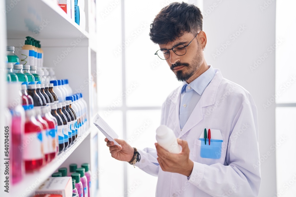 Young hispanic man pharmacist holding pills bottle reading preascription at pharmacy