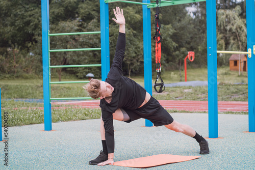 Blonde athlete warms up and stretches his body and major muscle groups to maximize training and minimize injury. When lunging forward, he pulls himself up by his upper arm. Yoga position