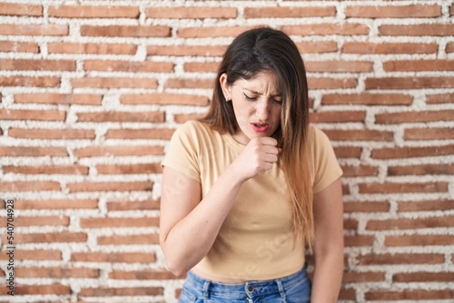 Young brunette woman standing over bricks wall feeling unwell and coughing as symptom for cold or bronchitis. health care concept. © Krakenimages.com