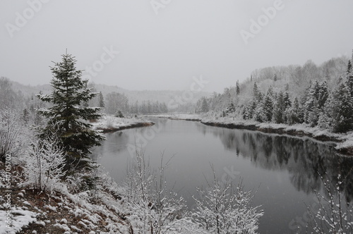 Winter Scenery Season Photo and Image. Horizontal Photo. Displaying its white blanket on trees, river and with a grey sky with a tranquillity feeling of peace.