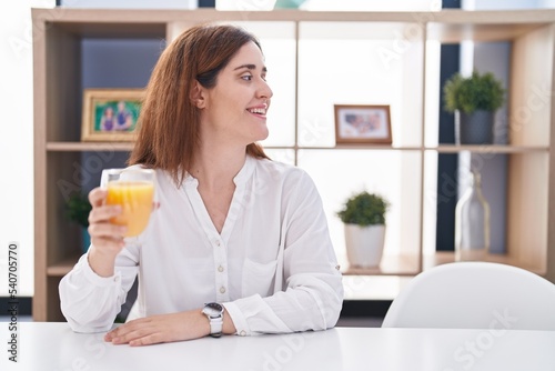 Brunette woman drinking glass of orange juice looking to side, relax profile pose with natural face and confident smile.