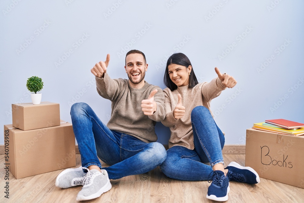 Young couple moving to a new home approving doing positive gesture with hand, thumbs up smiling and happy for success. winner gesture. Young couple moving to a new home approving doing positive gesture with hand, thumbs up smiling and happy for success. winner gesture.