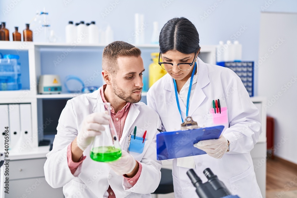Man and woman wearing scientists uniform measuring liquid at laboratory Man and woman wearing scientists uniform measuring liquid at laboratory