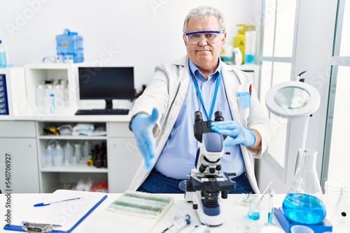 Senior caucasian man working at scientist laboratory smiling friendly offering handshake as greeting and welcoming. successful business.