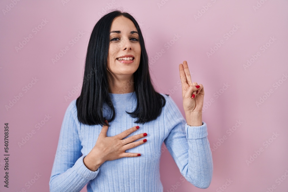 Hispanic woman standing over pink background smiling swearing with hand on chest and fingers up, making a loyalty promise oath Hispanic woman standing over pink background smiling swearing with hand on chest and fingers up, making a loyalty promise oath