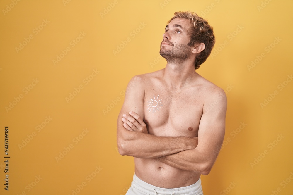 Caucasian man standing shirtless wearing sun screen looking to the side with arms crossed convinced and confident