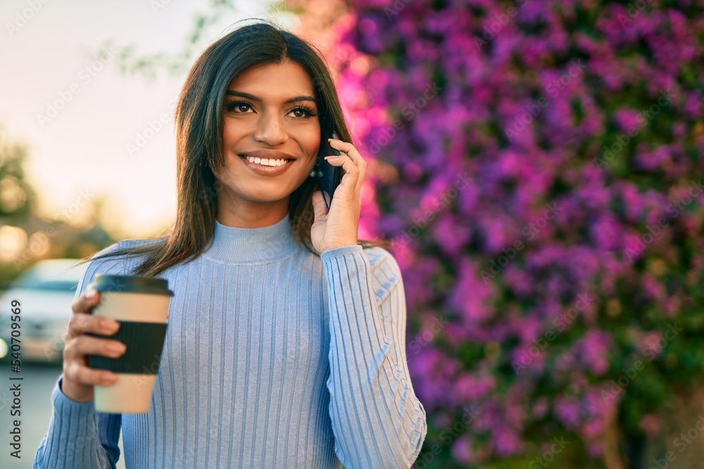 Young hispanic woman speaking on the phone and drinking a coffee by the park Young hispanic woman speaking on the phone and drinking a coffee by the park