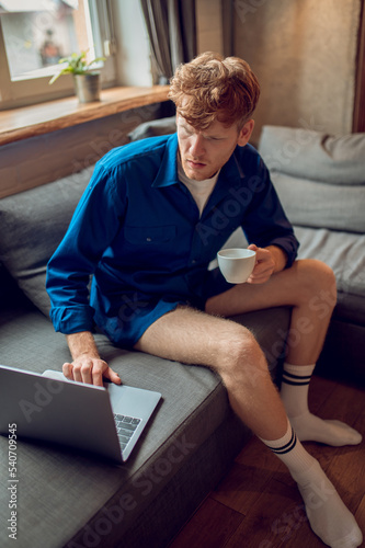 Young ginger man with a coffee mug in hand checking his email