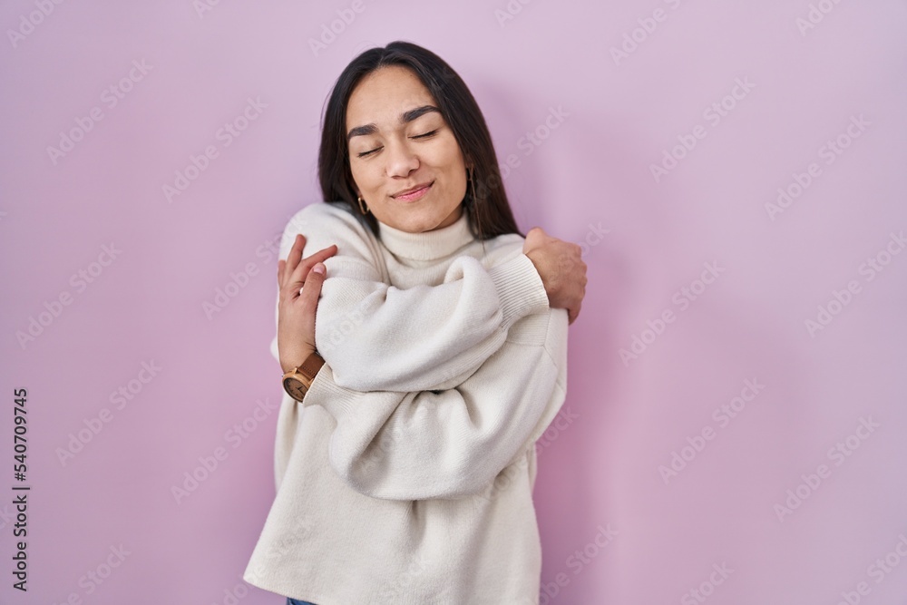 Young south asian woman standing over pink background hugging oneself happy and positive, smiling confident. self love and self care Young south asian woman standing over pink background hugging oneself happy and positive, smiling confident. self love and self care