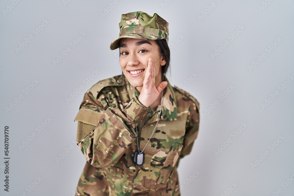 Young south asian woman wearing camouflage army uniform hand on mouth telling secret rumor, whispering malicious talk conversation
