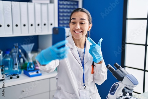 Young south asian woman working at scientist laboratory with smartphone smiling happy pointing with hand and finger