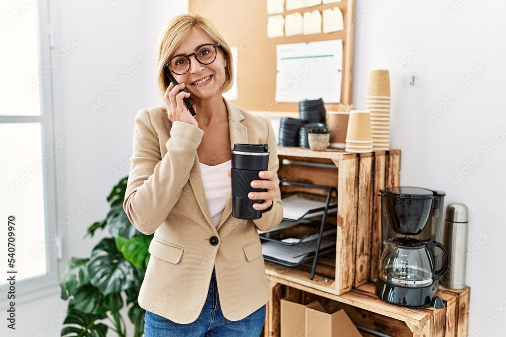 Middle age blonde woman talking on the smartphone drinking coffee at office Middle age blonde woman talking on the smartphone drinking coffee at office