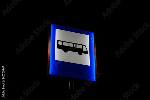 Close-up shot of an illuminated bus station signpost in the dark