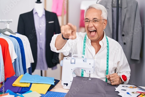 Middle age man with grey hair dressmaker using sewing machine pointing displeased and frustrated to the camera, angry and furious with you
