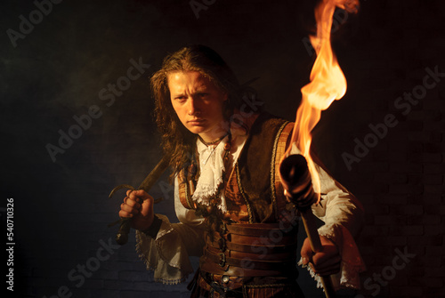 Young pirate filibuster with burning torch on dark brick background