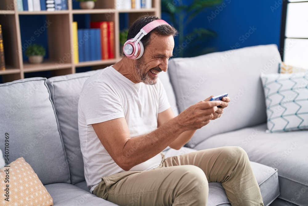 Middle age man playing video game sitting on sofa at home Middle age man playing video game sitting on sofa at home
