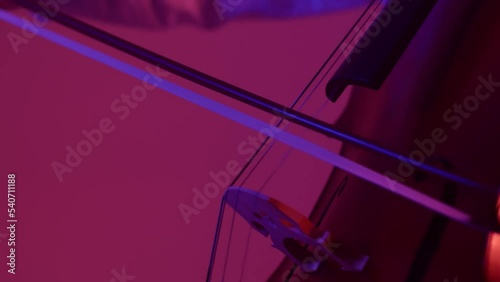 a woman in the orchestra plays the cello. a dark hall with purple light. the cellist leads the bow along the string. close up photo