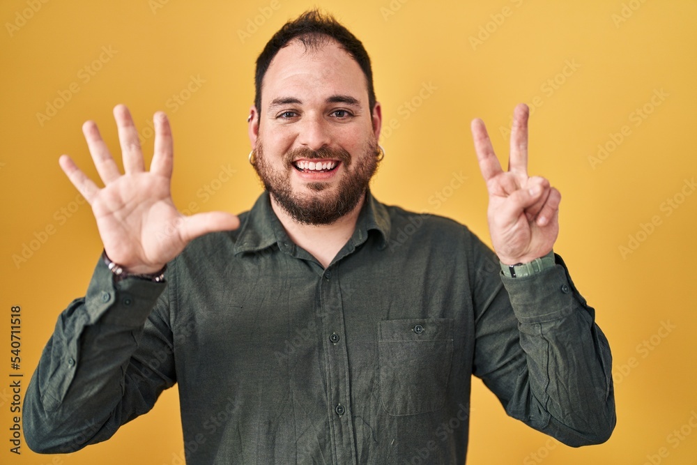 Plus size hispanic man with beard standing over yellow background showing and pointing up with fingers number seven while smiling confident and happy. Plus size hispanic man with beard standing over yellow background showing and pointing up with fingers number seven while smiling confident and happy.