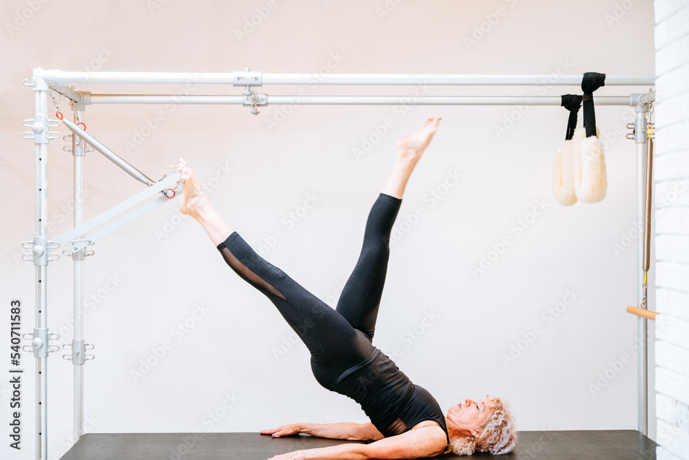 Series of pilates exercises of elderly woman workout in cadillac at fitness equipment at gym of rehabilitation center. Active and healthy life rehabilitation concept