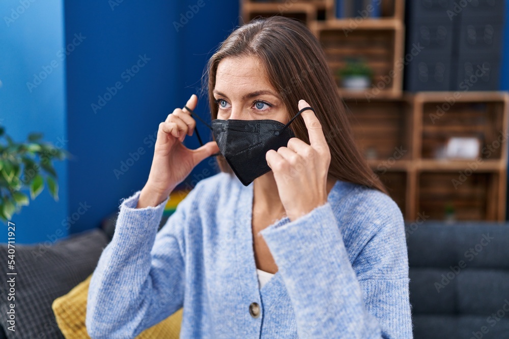 Young woman wearing medical mask sitting on sofa at home Young woman wearing medical mask sitting on sofa at home