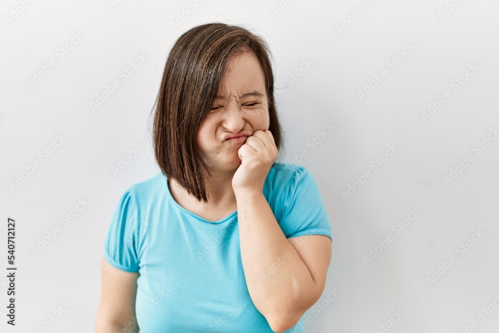 Young down syndrome woman standing over isolated background looking stressed and nervous with hands on mouth biting nails. anxiety problem. Young down syndrome woman standing over isolated background looking stressed and nervous with hands on mouth biting nails. anxiety problem.