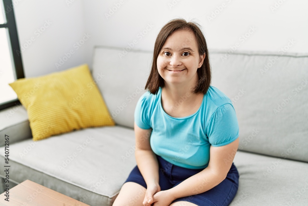 Brunette woman with down syndrome sitting on the sofa at the living room Brunette woman with down syndrome sitting on the sofa at the living room