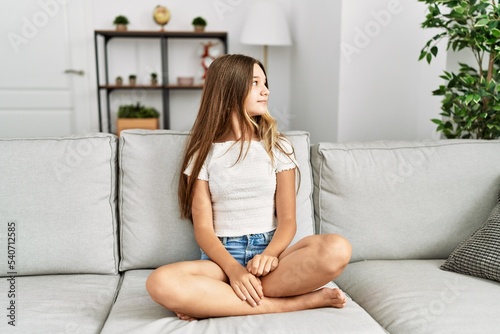 Young brunette teenager sitting on the sofa at home looking to side, relax profile pose with natural face with confident smile.