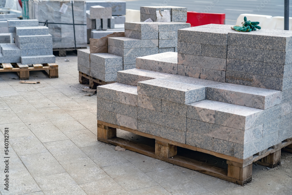 Many stacks of granite paving slabs on pallets for paving sidewalks located on a construction site near the road Many stacks of granite paving slabs on pallets for paving sidewalks located on a construction site near the road