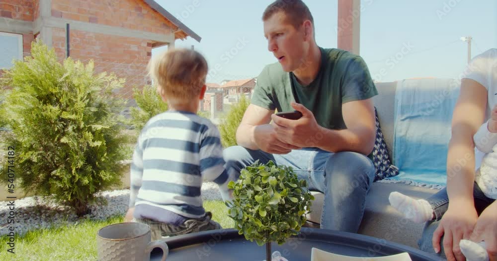 Father is talking and playing with his son while the mother is holding the baby Father is talking and playing with his son while the mother is holding the baby