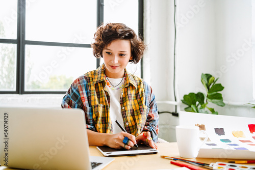 Smiling illustrator with graphics tablet using laptop at office