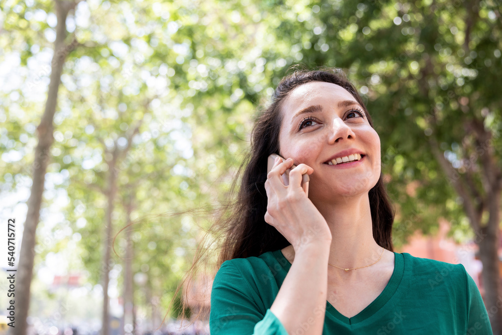 Happy woman talking on smart phone in front of tree Happy woman talking on smart phone in front of tree