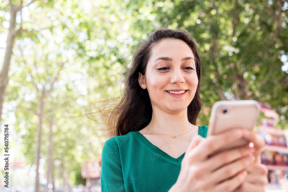 Happy woman using smart phone in front of trees