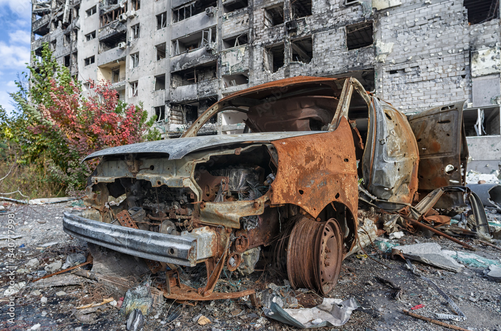 burnt blown up car against the background of a destroyed house in Ukraine