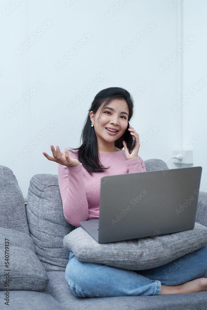 Portrait of a beautiful Asian teenage girl using her phone and computer sitting on the sofa at home Portrait of a beautiful Asian teenage girl using her phone and computer sitting on the sofa at home