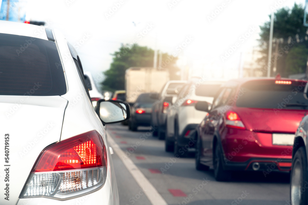 Rear side of white car on the asphalt road heading towards the goal of the trip. Traveling for work during rush hour. Environment blurred of other cars in the city. 