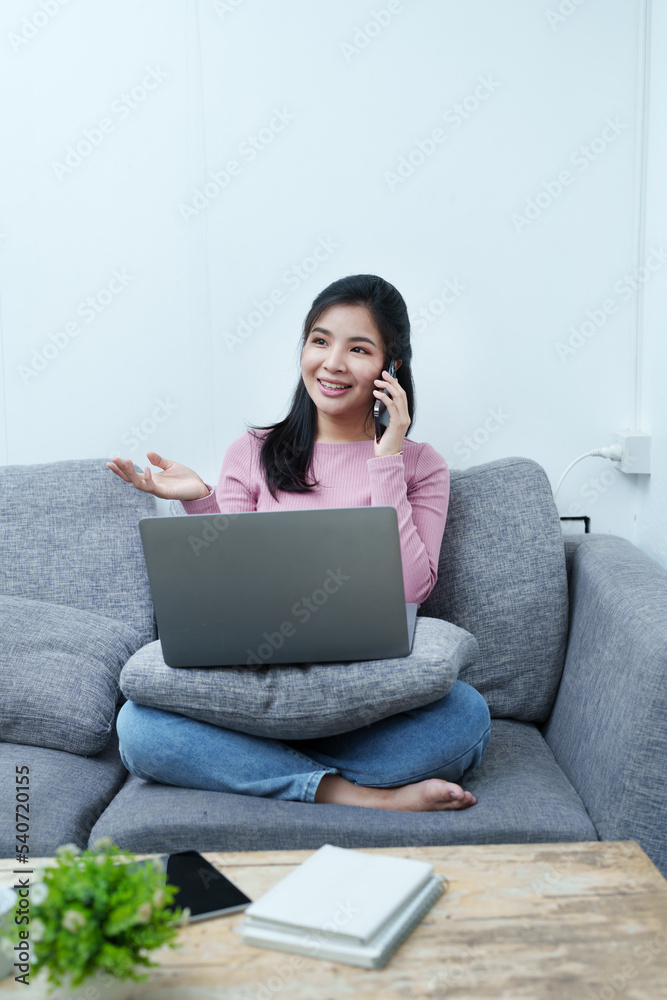 Portrait of a beautiful Asian teenage girl using her phone and computer sitting on the sofa at home Portrait of a beautiful Asian teenage girl using her phone and computer sitting on the sofa at home