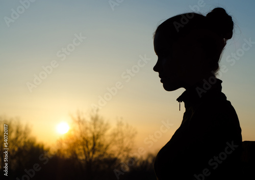 Silhouette of the beautiful young woman in the nature against clear sky and sun at spring sunset