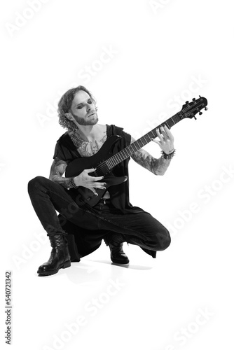 Portrait of stylish young man, rock musician, guitar player posing, playing over white background. Black and white photography