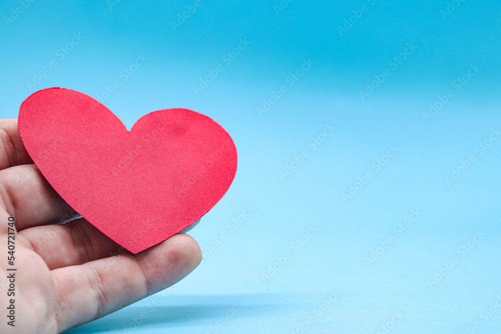 Fototapeta premium hands holding a red paper heart on a blue background. health care, hope, life insurance concept, world heart day, world health day, organ donor day, csr social responsibility, gratitude