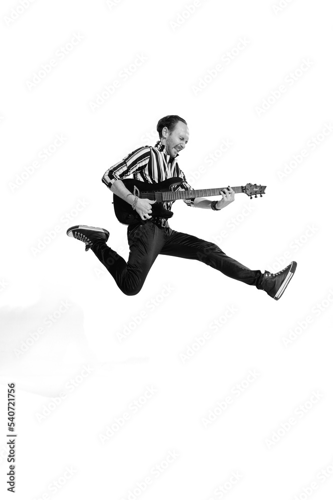 Portrait of young emotive man in stylish clothes playing guitar, posing isolated over white background. Black and white photo