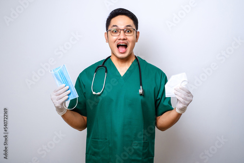 Cheerful young asian male doctor, nurse in scrubs, smiling and handing medical masks for patient safety