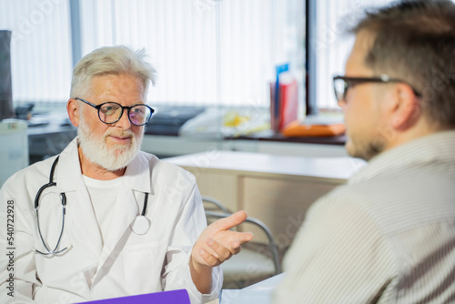 an elderly gray-haired male doctor in a medical office consults a male patient